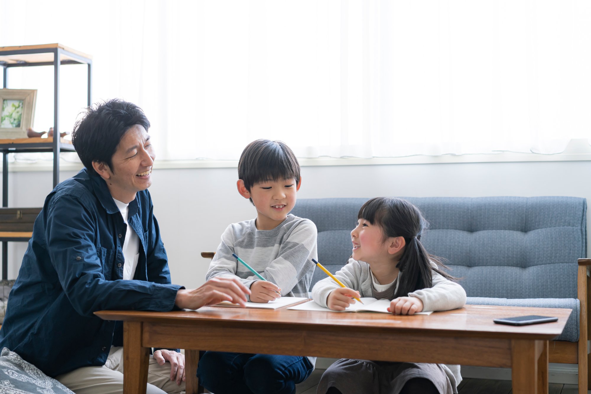 父親と子ども2人がリビングで楽しく勉強